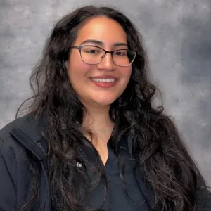Jacky has long dark hair and is standing in front of a grey backdrop